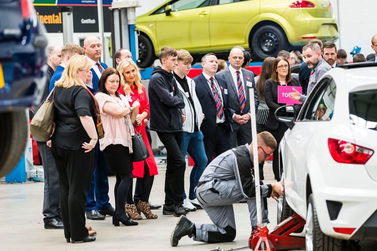 A group at a GTG open day watching and apprentice work on a car in the workshop