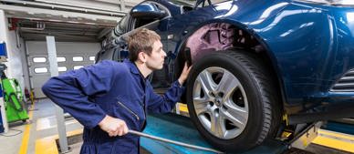 trainee inspecting behind a tyre on a car on a ramp